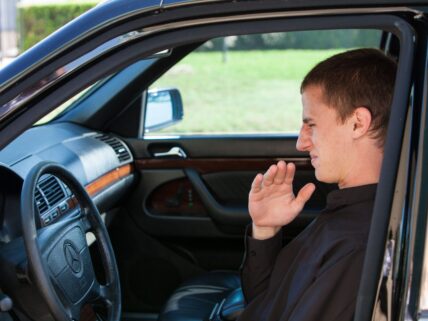 a man sitting in car making bad face because of odor in his car.